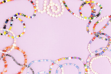 Necklaces and bracelets made from beads and pearls on a purple background. Border frame with copyspace. - obrazy, fototapety, plakaty