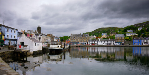 Fototapeta na wymiar On a grey and overcast afternoon in Tarbert, brightly painted houses and shops border the quay