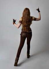 Full length portrait of beautiful young woman with long red hair, wearing steampunk inspired costume. Standing action pose isolated on studio background.
