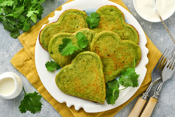 Spinach avocado pancakes in the shape of a heart with greek yogurt sauce and cherry tomatoes on white plate over light grey background. Breakfast food concept. Top view with copy space.