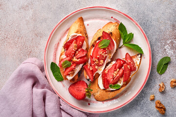 Open sandwiches with strawberries, soft cheese mint and walnut in ceramic plate on a light grey stone background. Summer and healthy dieting food, vegetarian food concept. Top view.