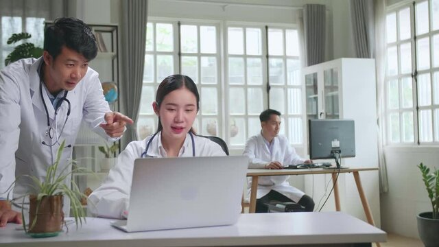 Hospital Medical Doctor'S Office: Two Asian Professional Physicians Talking, Consulting And Working On Laptop Computer. Specialists Discuss Patient Online Treatment, Writing Digital Medicine Prescript
