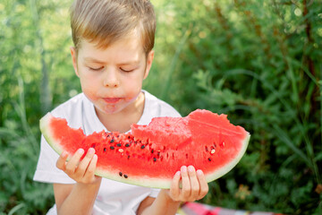 boy eating watermelon white t-shirt. Picnic with watermelons. The boy is holding a large piece of watermelon in his hands. Bright red juicy watermelon.