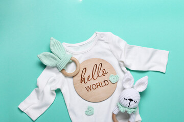 Close up of white baby bodysuit,eco wooden toys, beanbag and teethers, wooden tablet Hello World on mint background.Top view, flat lay.