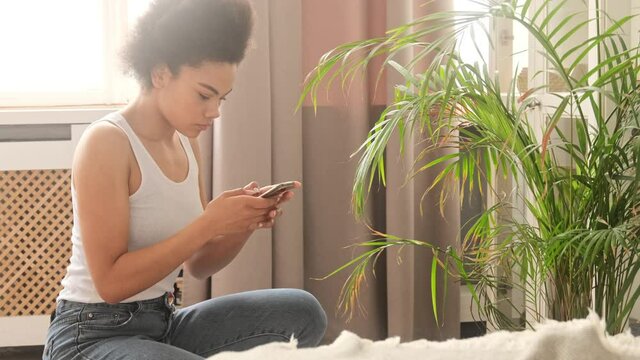 Young african american woman takes pictures photographing of a dry house plant uses a smart phone. Shares indoor plant leaves care in the mobile application.