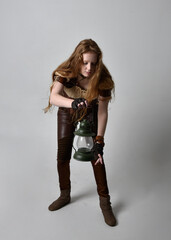 Full length  close up portrait of beautiful young woman with long red hair, wearing steampunk inspired costume holding  lantern  isolated on studio background.