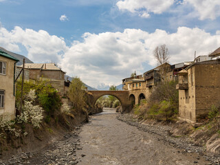 A mountain river flows under a bridge surrounded by yellow stone houses