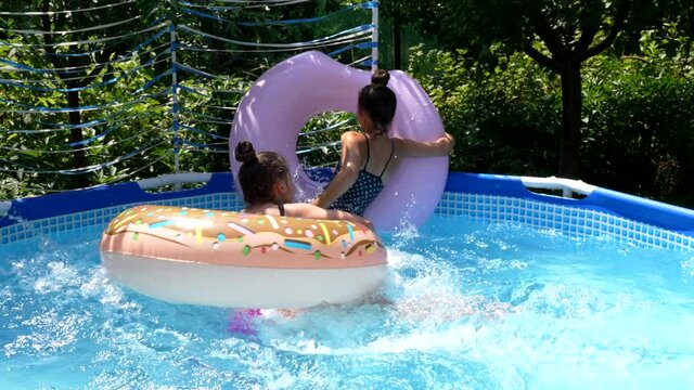 Happy girls have swimming pool fun with donut floats during summer vacation, waterplay
