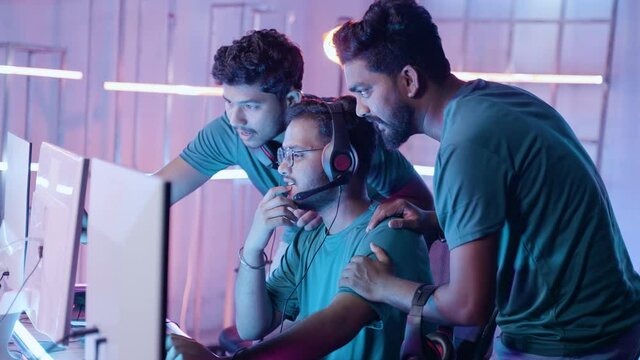 medium shot,Team of professional gamers discussing about game play by looking into monitor at esports championship league - concept of teamwork, strategy, togetherness and in multi-player tournament.