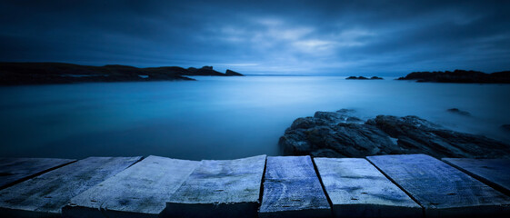 A wooden tabletop product display with a spooky coast background at dusk, night.