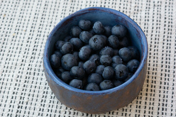 Top view of fresh farm ripe blueberries berries in a blue ceramic vintage cup on a light background. Copy space. Vegetarian breakfast