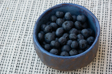 Breakfast mood. Fresh farm ripe blueberries berries in a blue ceramic crafts cup on a light background. Copy space. Vegetarian snack