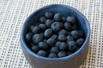 Close-up of fresh farm ripe blueberries in a blue ceramic vintage cup on a light background. Copy space. Vegetarian breakfast