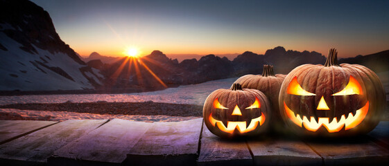 A mountain sunset with the spooky evil glowing eyes of Jack O' Lanterns on the right of a wooden...
