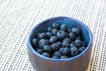 Fresh farm ripe blueberries berries in a blue ceramic handmade cup on a light background. Breakfast mood. Copy space. Vegetarian snack