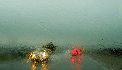 Defocussed traffic viewed through a car windscreen covered in rain,. Focus on raindrops. This is in the fall