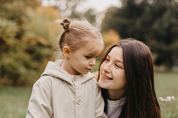 Young happy and smiling mom with her little daughter in arms hugging and kissing spending a weekend...