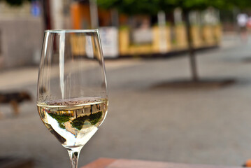Glass of white wine close up. Alcoholic drink on a wooden table on a background of the city. Transparent wine on the summer terrace of the restaurant.