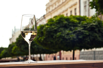 Glass of white wine close up. Alcoholic drink on a wooden table on a background of the city. Transparent wine on the summer terrace of the restaurant.