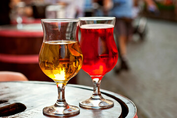 Glass of red and white wine close up. Alcoholic liqueur on a wooden barrel on a background of the city. Blurred people in the background.