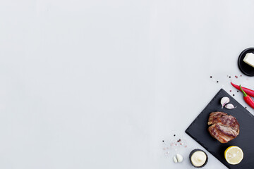 Gray background flat lay with cut of red rib-eye meat on black cutting board
