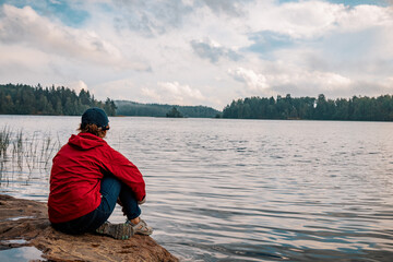 A thoughtful girl is sitting on the shore of the lake. Contemplation of the beautiful nature.