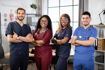 Diverse multiethnic cheerful medical team at work in hospital. Four multiracial colleagues healthcare workers, medical students. Mixed-races physicians and nurses looking at camera. Clinic team. - Powered by Adobe