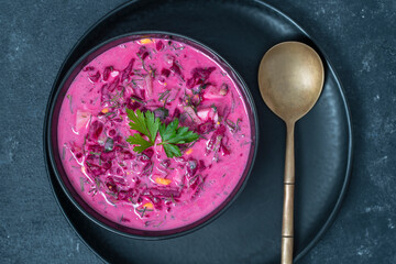 Delicious cold summer beetroot soup with cucumber, boiled egg, radish in black bowl on table