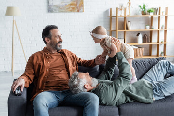 Cheerful same sex couple holding baby daughter on couch in living room