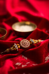 Raksha Bandhan background with an elegant Rakhi and Rice Grains on red cloth textured background.