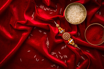 Raksha Bandhan background with an elegant Rakhi and Rice Grains on red cloth textured background.