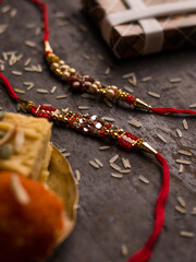 Raksha Bandhan background with an elegant Rakhi and Rice Grains on dark textured background.