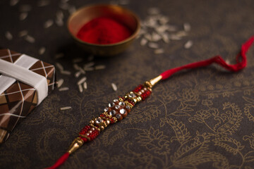 Raksha Bandhan background with an elegant Rakhi and Rice Grains on dark textured background.