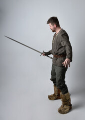 Full length  portrait of  young handsome man  wearing  medieval Celtic adventurer costume.  Standing pose holding a sword, isolated on studio background.