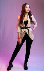 young beautiful girl posing on a colored background. teenager in black pants, boots and beige jacket in model poses