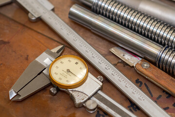 Close up scene of dial vernier caliper and the machine parts on the work bench.