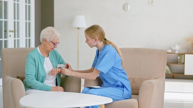Skilled nurse puts blood pressure monitor on old woman hand