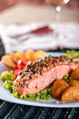 Um pedaço de salmão assado grelhado pimenta limão batata rustica e sal em um prato com folhas de alface e tomate cereja. fundo de tijolos rusticos
e vinha branco
