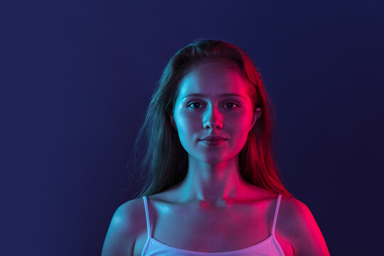 Portrait of young beautiful girl isolated on dark blue studio background in pink neon light. Concept of human emotions, facial expression, youth, sales, ad.