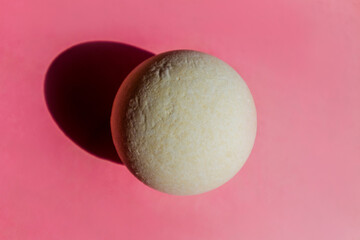 
White round bath bomb on a pink background. The rough texture of the bath bomb. Bathroom accessories.