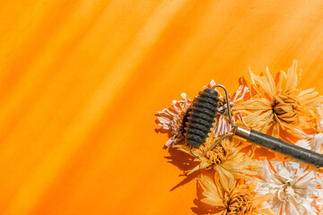 
A green jade facial massager lies among dry flowers on a yellow background with sunbeams. Anti-aging facial massager.