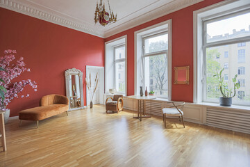 antique vintage interior in 19th century style living room with bright red walls, wood floor and direct sunlight inside the room.