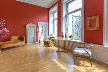 antique vintage interior in 19th century style living room with bright red walls, wood floor and direct sunlight inside the room.