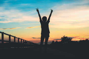 Fototapeta premium Happy celebrating winning success woman at sunset or sunrise standing elated with arms raised up.