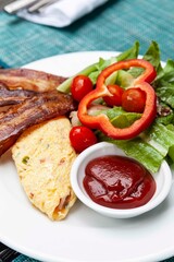 Western breakfast, scrambled eggs, bacon and fresh vegetables with tomato sauce