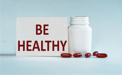 On a light blue background a card with the text BE HEALTHY near the white bottle pills.