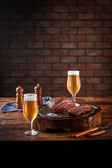 Grilled cap rump steak on wooden cutting board with two sweaty cold tulipa glasses of beer. Wooden table and bricks wall background (Brazilian picanha).