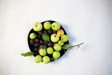 plum and apple on plate on white wooden table