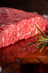 Closeup of marble denver beef on a wood resined cutting board with rosemary branch.