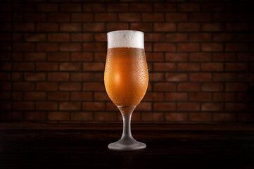 Isolated sweaty tulipa glass of refreshing pilsen draft beer with brick wall background.